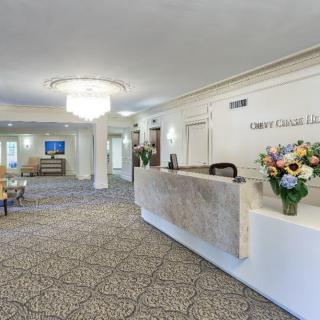 A well-lit hotel lobby featuring a reception desk with floral arrangements and a chandelier.