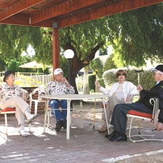 A group of people sitting and talking at a table under a shaded patio.