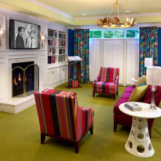 A vibrant and cozy living room featuring a fireplace, striped chairs, and a TV with classic black-and-white movies.