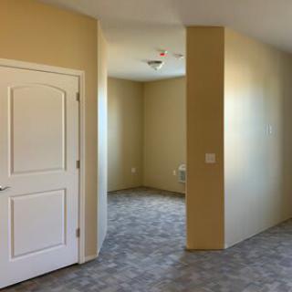 A vacant room with beige walls, a white door, and carpeted flooring.