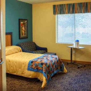 A cozy hotel room featuring a single bed, a side table, a lounge chair, and a window with blinds.