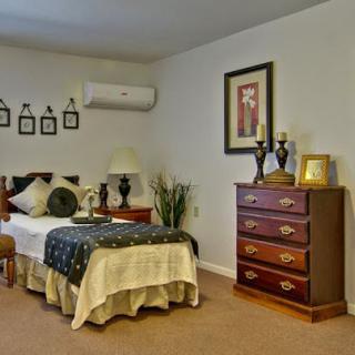 A cozy bedroom featuring a bed with decorative pillows, a wooden dresser, and framed artwork on the wall.