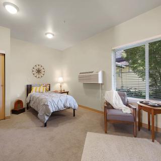 A cozy bedroom with a bed, chairs, and a large window letting in natural light.