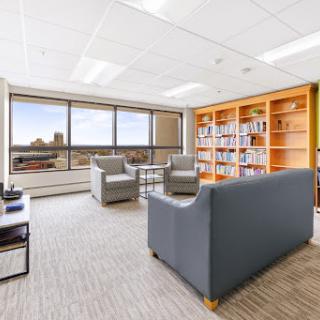 A serene office space featuring comfortable seating, a bookshelf filled with books, and large windows offering a city view.