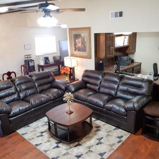 A cozy living room with two leather couches and a central coffee table, complemented by an area rug and a ceiling fan for comfort.