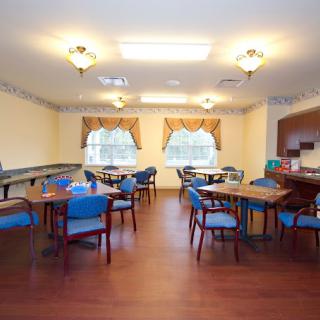 A well-lit dining area with multiple tables and chairs, featuring wooden floors and decorated windows.