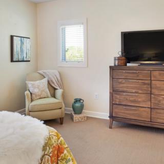 A cozy bedroom with a chair, dresser, and television.