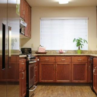 A modern kitchen with wooden cabinets, stainless steel appliances, and a window with blinds.