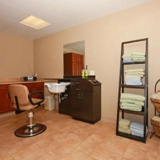 Interior of a salon with a chair, sink, mirror, and neatly stacked towels on shelves.