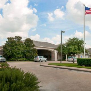 A building with a parking lot, surrounded by trees and an American flag under a cloudy sky.