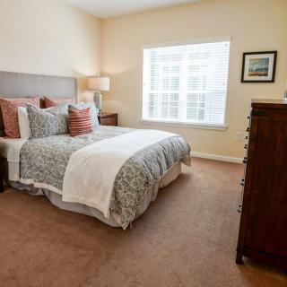 A cozy bedroom with a neatly made bed, featuring decorative pillows and a bedside lamp.