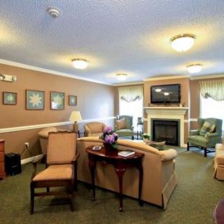 A cozy living room with comfortable sofas and armchairs arranged around a fireplace and television, decorated with wall art and a carpeted floor.