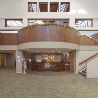 A spacious reception area with wood paneling and a central desk, flanked by staircases.