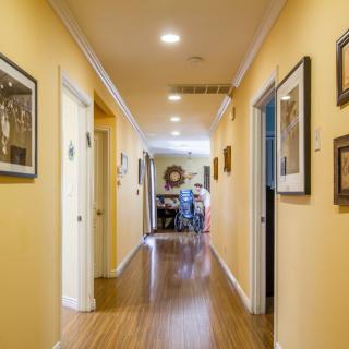 A well-lit hallway with yellow walls adorned with artwork, leading to a room at the end.