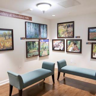 An art gallery room featuring various framed paintings on the walls and seating benches in the center.