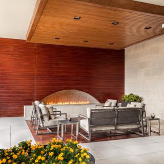 A modern outdoor seating area with a fireplace, featuring stylish patio furniture and wood paneling.