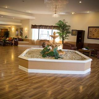 A spacious lobby area featuring a central fountain and indoor plants with a wooden floor.