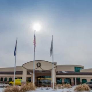 A building with flags in front, under a cloudy sky with the sun shining, surrounded by snow.