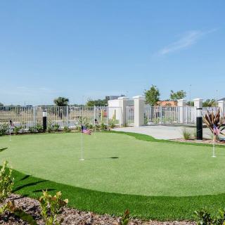 A sunny day at a well-maintained outdoor putting green, surrounded by a landscaped area.