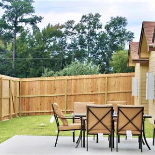 A serene outdoor patio space with dining furniture, surrounded by a wooden fence and greenery.