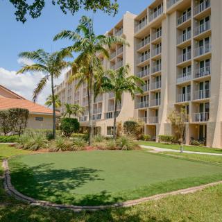 A view of an apartment complex with palm trees and a grassy courtyard under a clear blue sky.