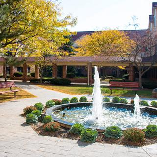 A serene courtyard featuring a central fountain surrounded by greenery and trees with autumn foliage.