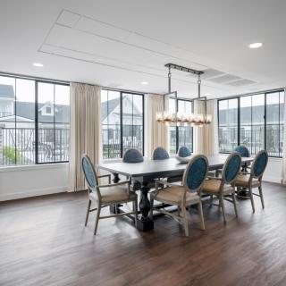 A spacious dining room featuring a large table with elegant chairs, surrounded by large windows and highlighted by a modern chandelier.