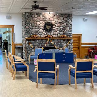 A cozy waiting area featuring wooden chairs arranged around a stone fireplace.