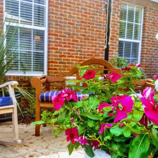 A cozy outdoor garden area with vibrant flowers and benches against a brick wall backdrop.