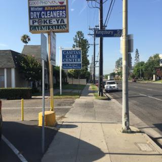 A view of a street featuring signs for day cleaners and a clear sidewalk, with vehicles parked along the road.