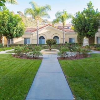 A well-maintained house with a lush green lawn and palm trees lining the pathway.