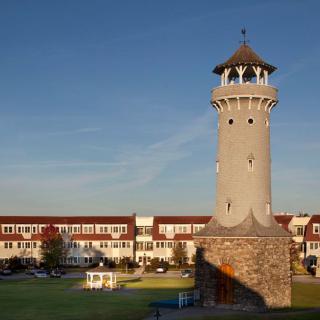 A lighthouse tower stands prominently against a clear sky, surrounded by residential buildings.