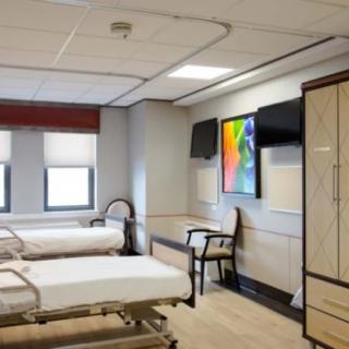 A hospital room featuring two beds, chairs, and a colorful artwork on the wall.