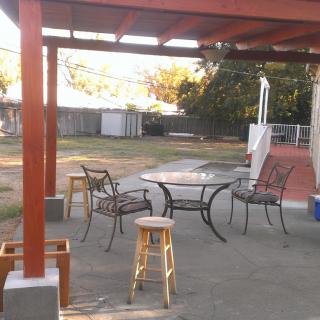 An outdoor patio area with a table and chairs under a pergola, set in a backyard.