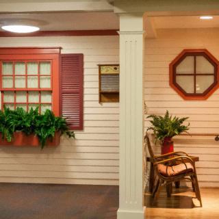 A cozy indoor porch area featuring a rocking chair, potted plants, and decorative windows with shutters.