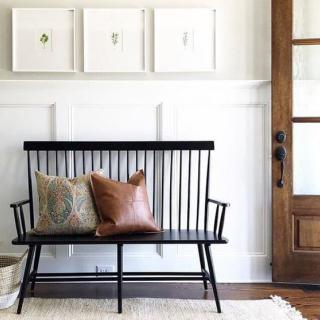 A minimalist entryway features a black bench with decorative cushions and framed wall art.