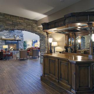 A cozy living space featuring a wooden bar, stone archway, and a warm fireplace.