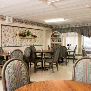 A cozy dining area with floral wallpaper, furnished with round tables and cushioned chairs.