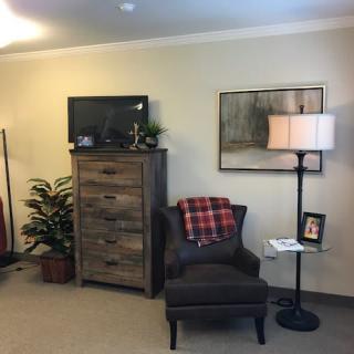 A cozy living room corner with an armchair, lamp, and a wooden dresser topped with a television.