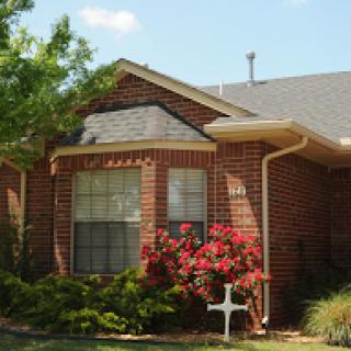 A charming brick house surrounded by lush greenery and blooming flowers.