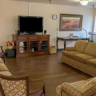 A cozy living room featuring a television, sofas, chairs, and a wooden floor with wall art.
