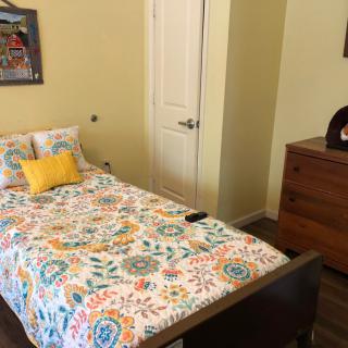 A bedroom with a single bed featuring a colorful floral bedspread, a dresser, and a closed door.