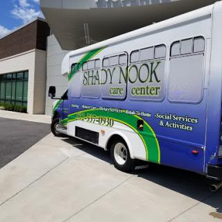 A bus for Shady Nook Care Center parked outside a modern building.