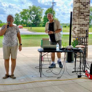 Two people are hosting an event outdoors with electronic equipment on a table.