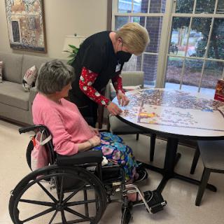 A caregiver assists an elderly person in a wheelchair with an activity at a care facility.