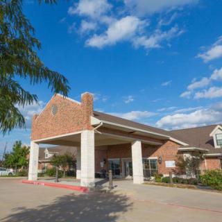 A brick building entrance under a clear blue sky with scattered clouds.