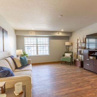 A cozy living room with hardwood floors and modern furniture, featuring a sofa, bookshelf, and large window.