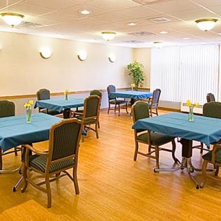 A well-lit dining area with multiple tables and chairs, featuring blue tablecloths and a hardwood floor.