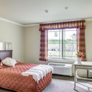 A cozy bedroom with a single bed, plaid curtains, and a small desk by the window.