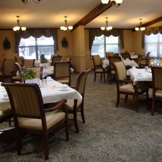 A cozy dining room with neatly arranged tables and chairs, featuring warm lighting and elegant decor.